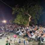 Θέα προς την πλατεία από το Ιατρείο. Η πλατεία είναι γεμάτη κόσμο και στον δρόμο χορεύουν.