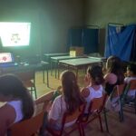 παιδάκια κάθονται στις καρέκλες και βλέπουν ταίνα που προβάλεται στον τοίχο μέσα στο σχολείο